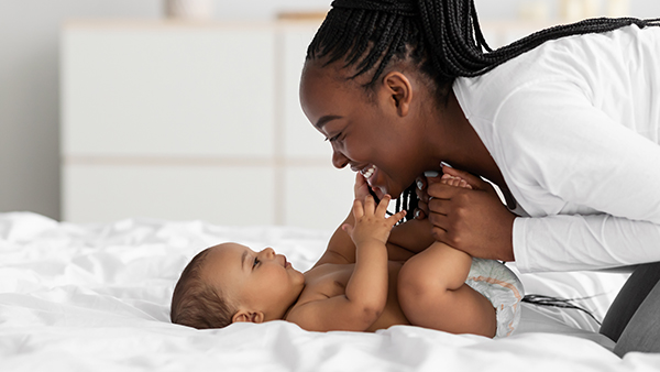 Mom playing with baby lying on back on bed.